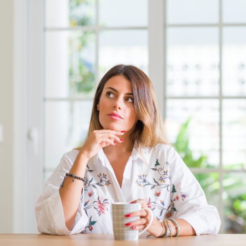 Young woman at home drinking coffee serious face thinking about question, very confused idea